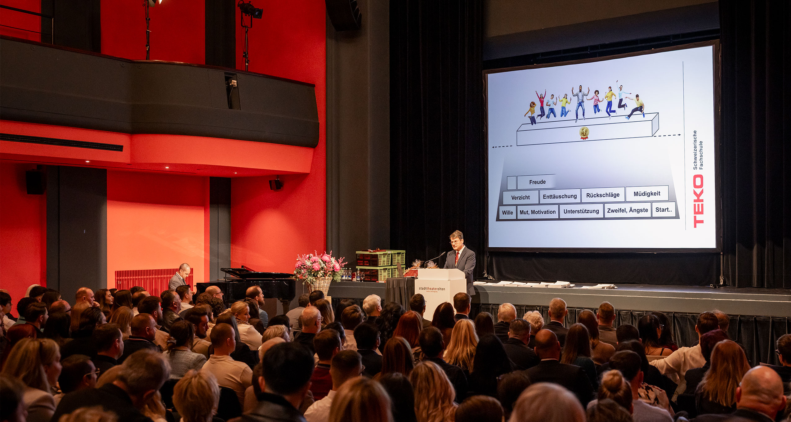 Moderator eröffnet einen Firmenanlass auf einer beleuchteten Bühne vor Publikum.