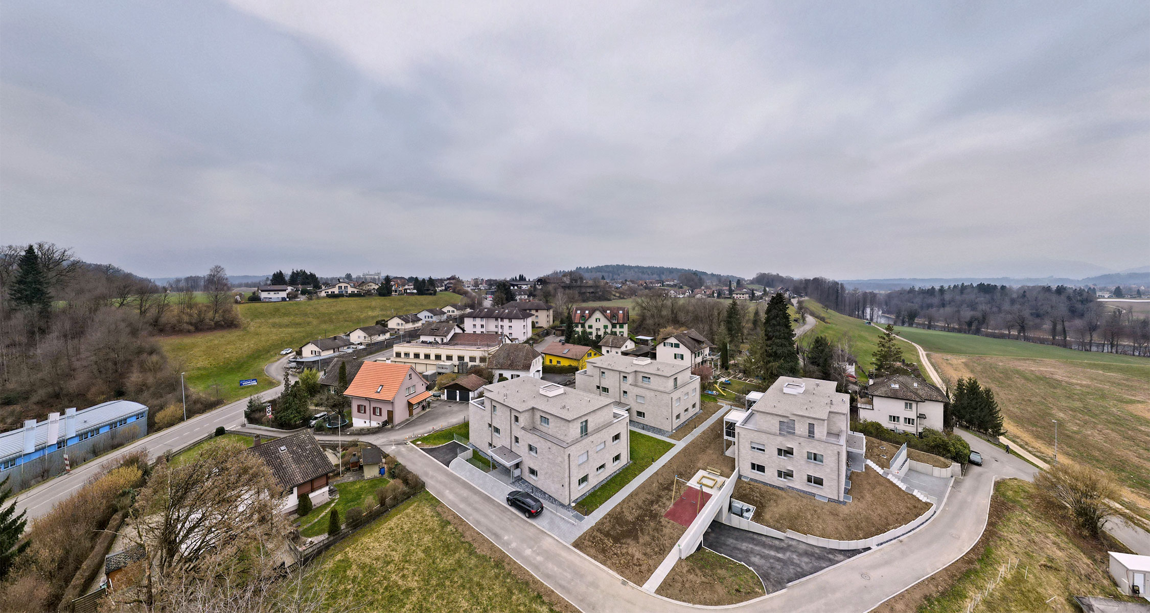 Drohnenaufnahme einer modernen Wohnüberbauung mit mehreren Mehrfamilienhäusern und umliegender Landschaft im Aargau.