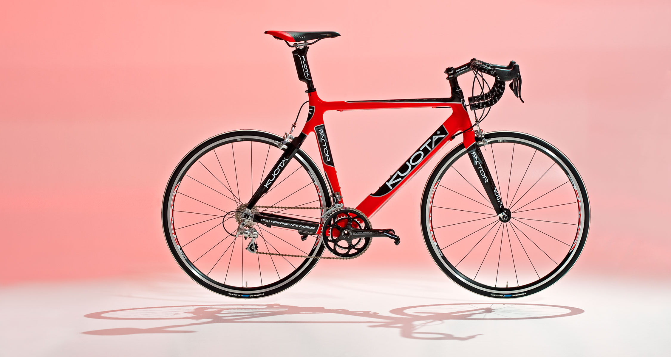 Rotes Carbon-Rennvelo als professionelle Produkt- und Werbeaufnahme vor einem rosa Studiohintergrund.