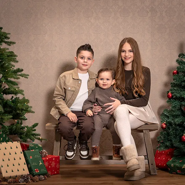 Stimmungsbeispiel aus einem Weihnachtsshooting in Zofingen mit drei Kindern auf einer Bank zwischen Weihnachtsbäumen und Geschenken.